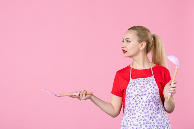 Free photo front view young housewife  holding cutlery on pink wall
