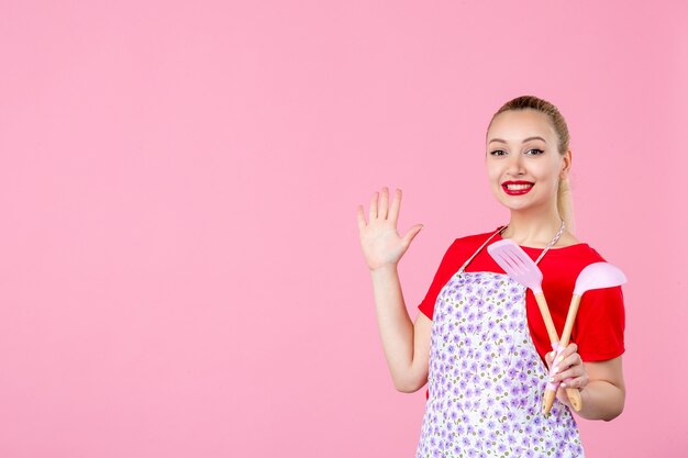 Вид спереди молодая домохозяйка держит столовые приборы на розовой стене