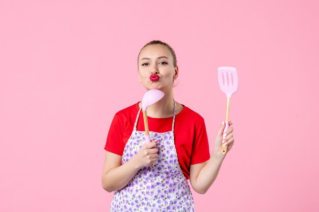 Front view young housewife holding cutlery on pink wall