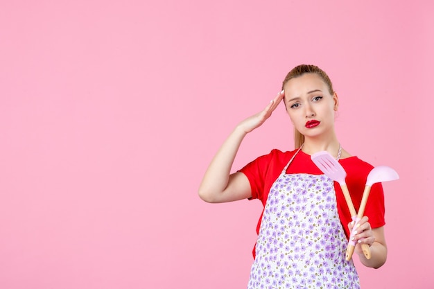 Front view young housewife holding cutlery on pink wall