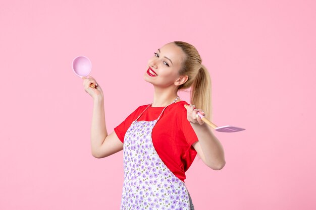 Front view young housewife holding cutlery on pink wall