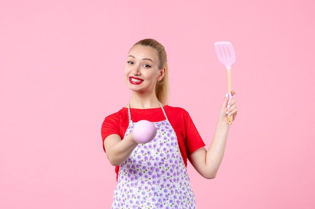 Front view young housewife holding cutlery on pink wall