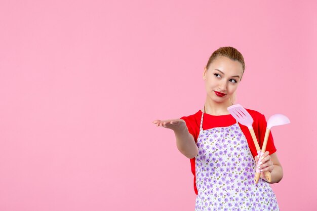 Front view young housewife holding cutlery on pink wall