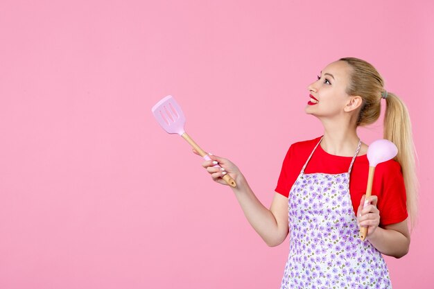 Front view young housewife holding cutlery on pink wall