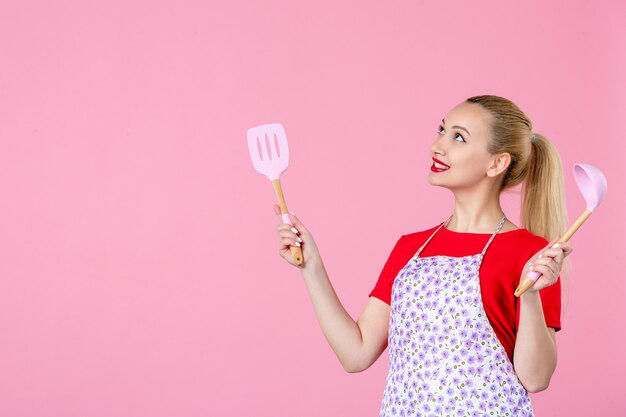 Front view young housewife holding cutlery on pink wall