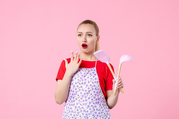 Front view young housewife posing with cutlery in her hands on pink wall