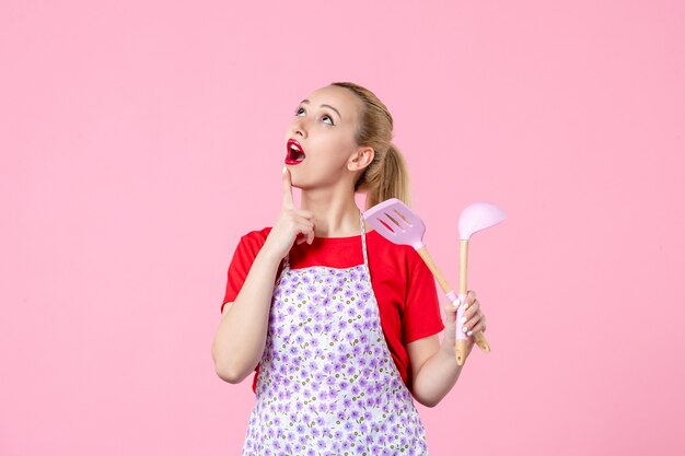 Front view young housewife posing with cutlery in her hands on pink wall