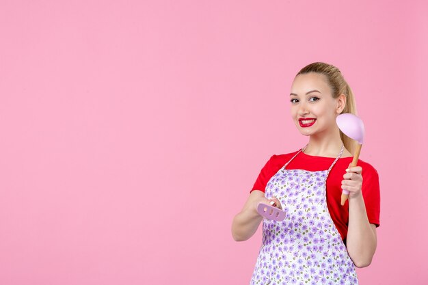 Front view young housewife posing with cutlery in her hands on pink wall