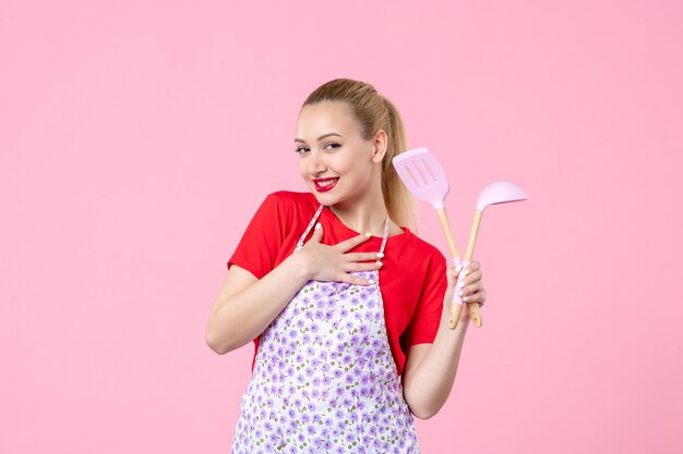 Front view young housewife posing with cutlery in her hands on pink wall