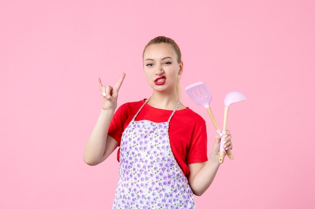 Front view young housewife posing with cutlery in her hands on pink wall