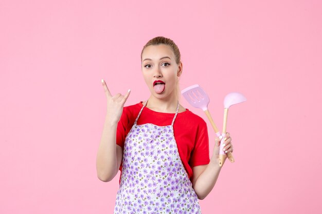 Front view young housewife posing with cutlery in her hands on pink wall