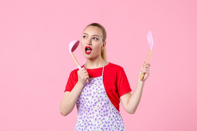 Front view young housewife posing with cutlery on pink wall