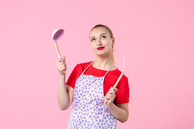 Front view young housewife posing with cutlery on pink wall