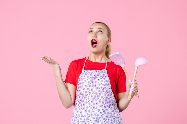 Front view young housewife posing with cutlery on pink wall