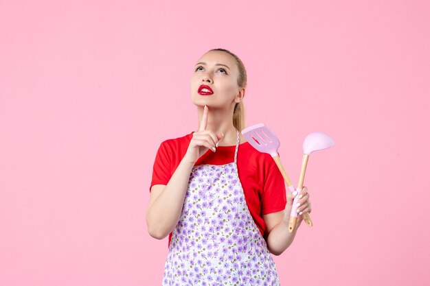 Front view young housewife posing with cutlery on pink wall