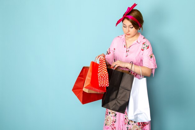 A front view young lady in flower designed pink dress holding shopping packages on blue