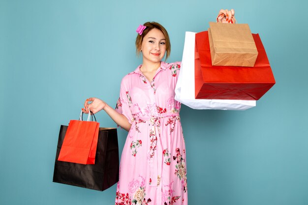 花の正面の若い女性は、ショッピングパッケージを保持し、青に笑みを浮かべてピンクのドレスを設計