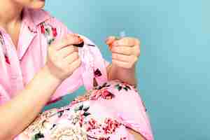 Free photo a front view young lady in flower designed pink dress painting her nails on blue