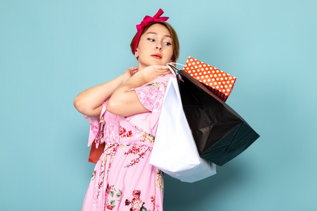 A front view young lady in flower designed pink dress posing holding shopping packages on blue