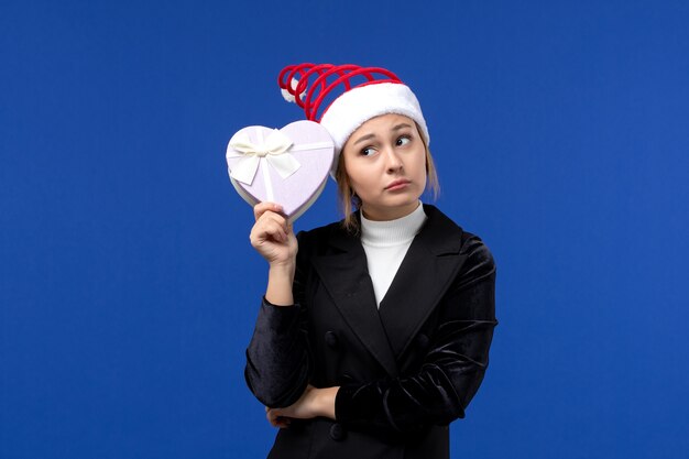 Front view young lady holding heart shaped present on blue wall new year holiday gifts