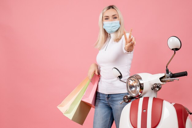 Front view young lady holding shopping bags gesturing victory sign near moped