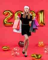 無料写真 赤のショッピング バッグの風船を保持している黒のドレスを着た正面の若い女性