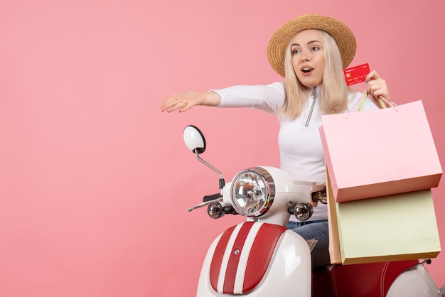 Front view young lady on moped holding card and shopping bags
