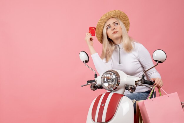 Front view young lady on moped holding credit card thinking something