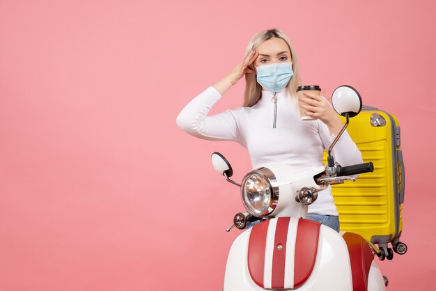 Front view young lady on moped with yellow suitcase holding coffee cup