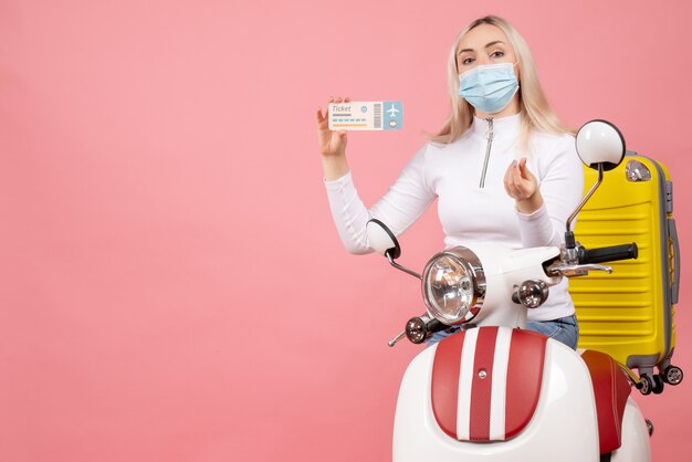 Front view young lady on moped with yellow suitcase holding ticket making money sign