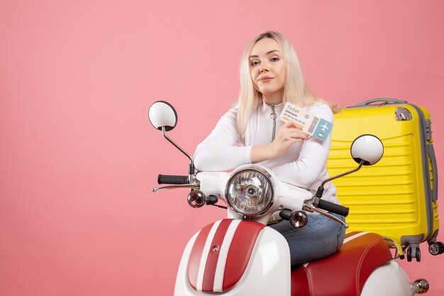 Front view young lady on moped with yellow suitcase holding ticket