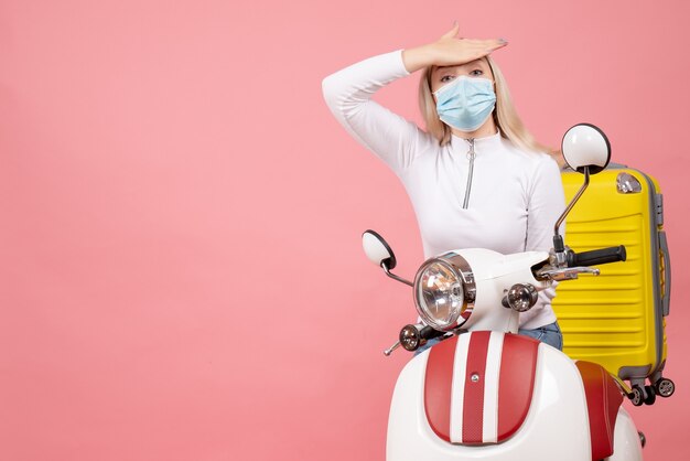 Front view young lady on moped with yellow suitcase putting hand on her forehead