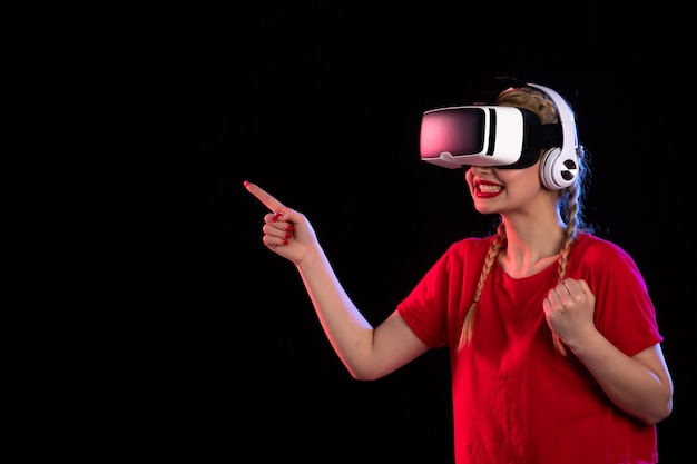 Front view of young lady playing vr in headphones on dark wall