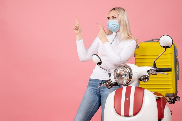 Front view young lady pointing at ceiling standing near moped