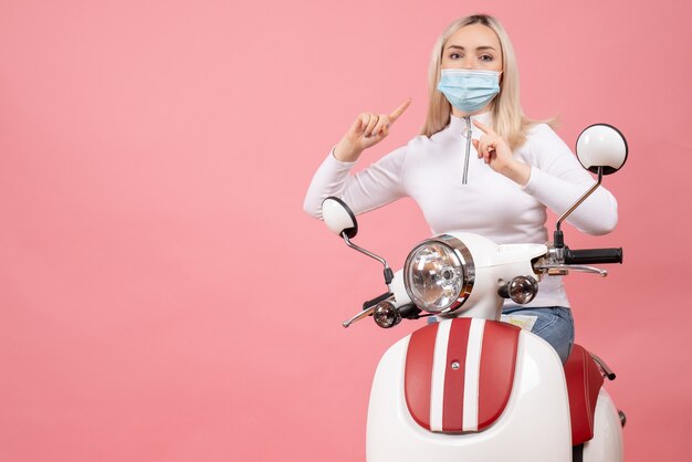 Front view young lady pointing at mask standing near moped