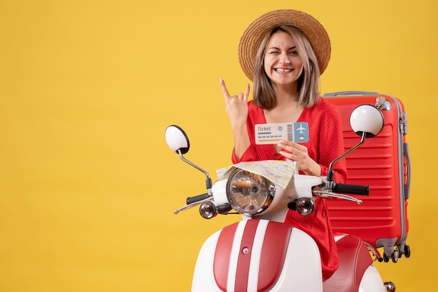 Front view young lady in red dress holding ticket making rock sign on moped