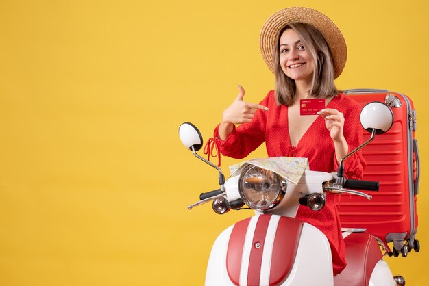 Front view young lady in red dress pointing at bank card on moped