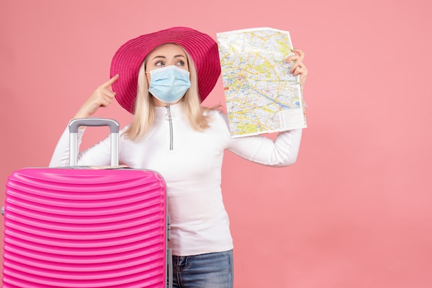 Front view young lady standing near suitcase holding map pointing at something