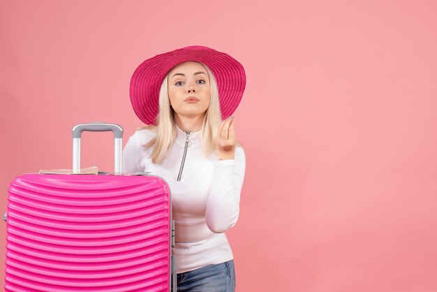 Front view young lady standing near suitcase making tasty sign