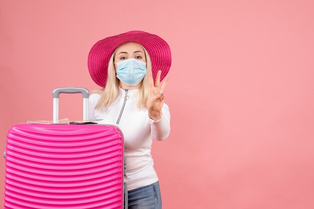 Front view young lady standing near suitcase showing three fingers