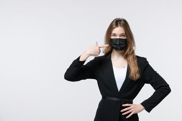 Front view of young lady in suit wearing surgical mask and pointing something on the left side on white