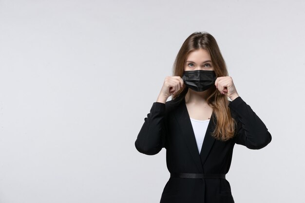 Front view of young lady in suit wearing surgical mask and posing for camera on white