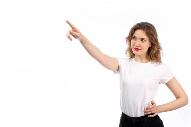 A front view young lady in white shirt and black modern jeans pointing into the distance on the white