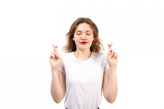 A front view young lady in white shirt and black modern jeans wishing on the white