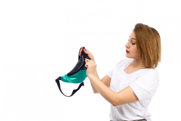 A front view young lady in white shirt and light modern trousers fixing little bag on the white