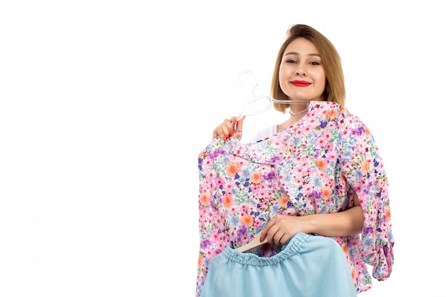 A front view young lady in white shirt and light modern trousers holding blue skirt and blouse on the white