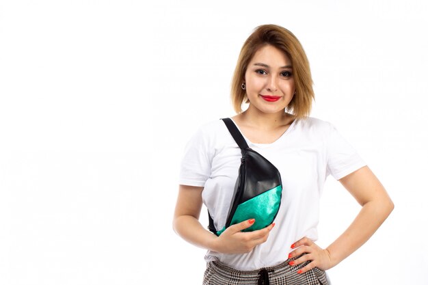 A front view young lady in white shirt and light modern trousers wearing little bag smiling on the white