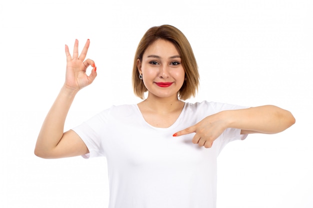 A front view young lady in white shirt posing smiling showing alright sign on the white