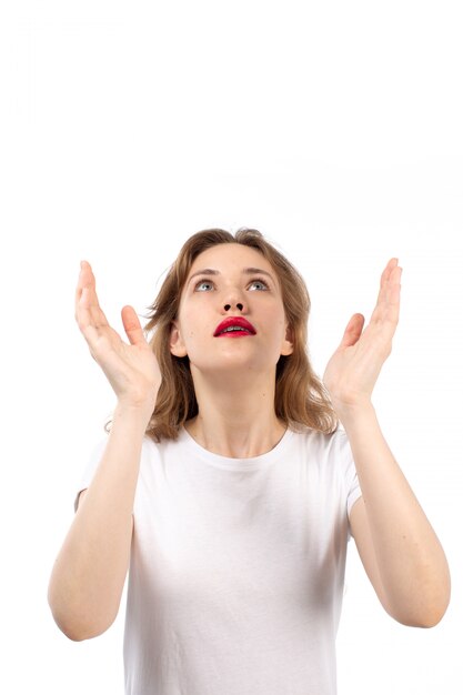 A front view young lady in white t-shirt posing surprised excited looking into the skies on the white