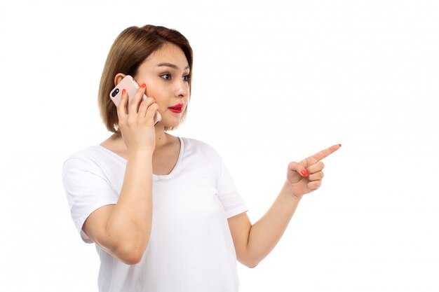 Вид спереди молодая леди в белой футболке позирует говорить по телефону на белом